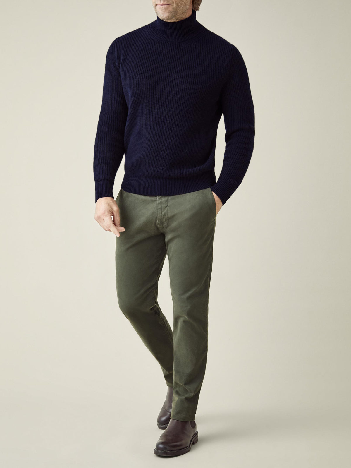 A front view of a model wearing the Chunky Knit Mock Neck in Midnight Blue with olive green trousers and brown boots.