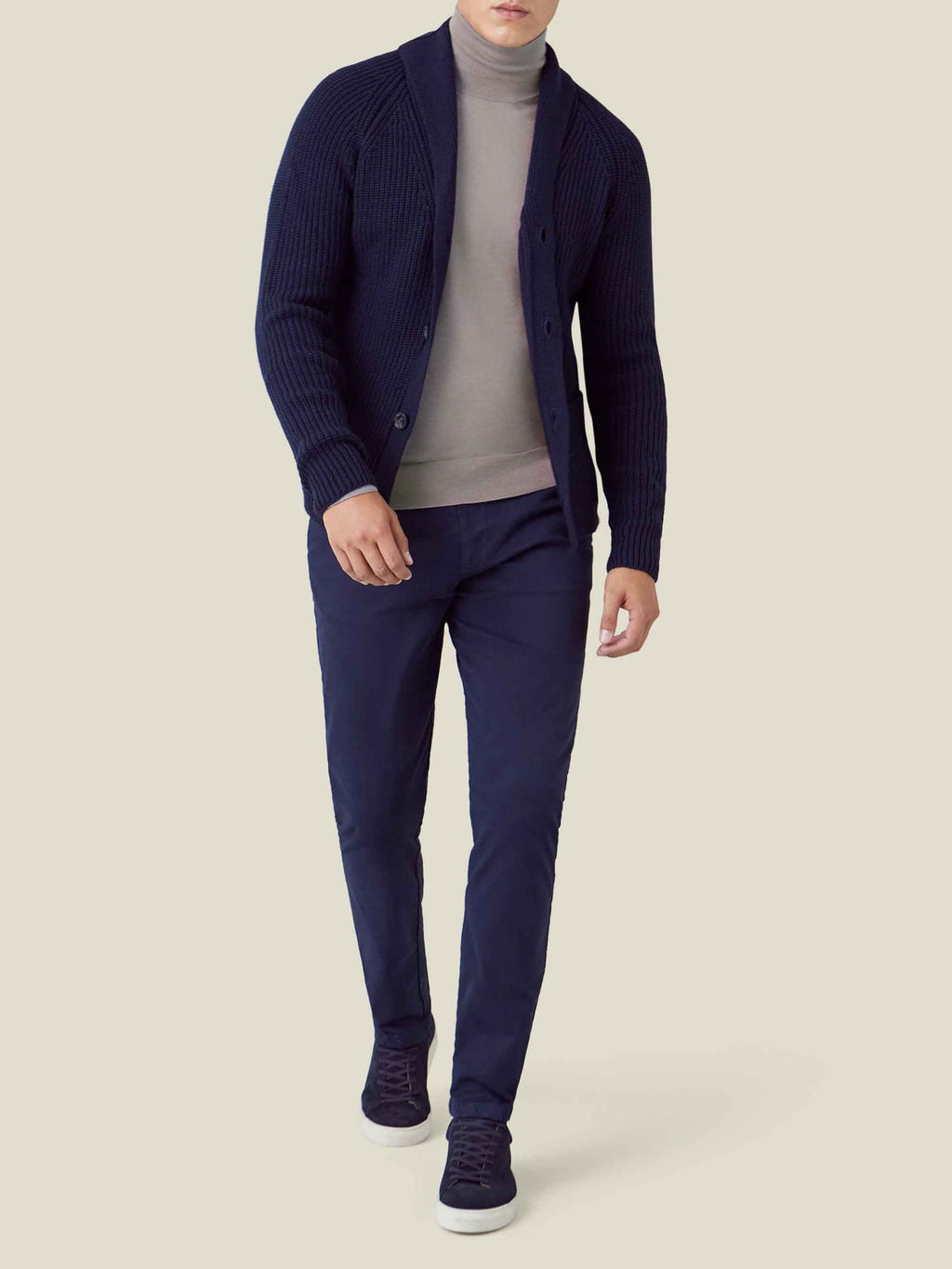 A model wears Luca Faloni's Silk-Cashmere Mock Neck in Nocciola Brown, under a navy cardigan with navy trousers and sneakers.