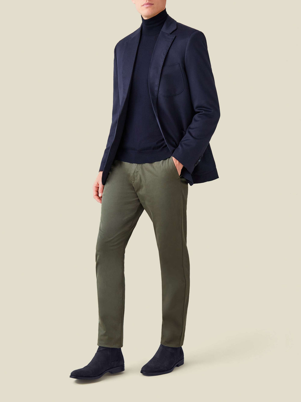 A model wears the Navy Blue Silk-Cashmere Mock Neck layered under a navy blazer with olive trousers and navy suede boots.