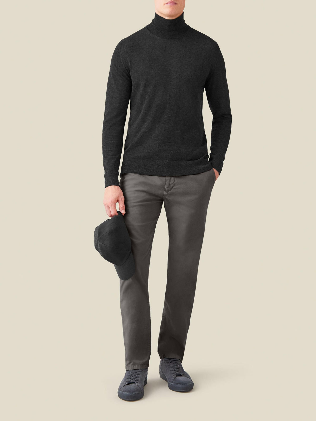 A model wears the Luca Faloni Silk-Cashmere Mock Neck in Charcoal Grey, paired with grey trousers, sneakers and a black cap.