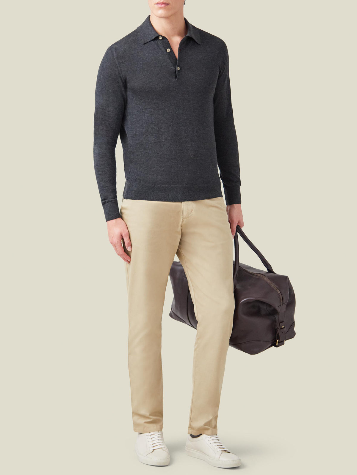 Full-body view of a model wearing Luca Faloni's charcoal grey silk-cashmere polo with beige chinos and a leather travel bag.