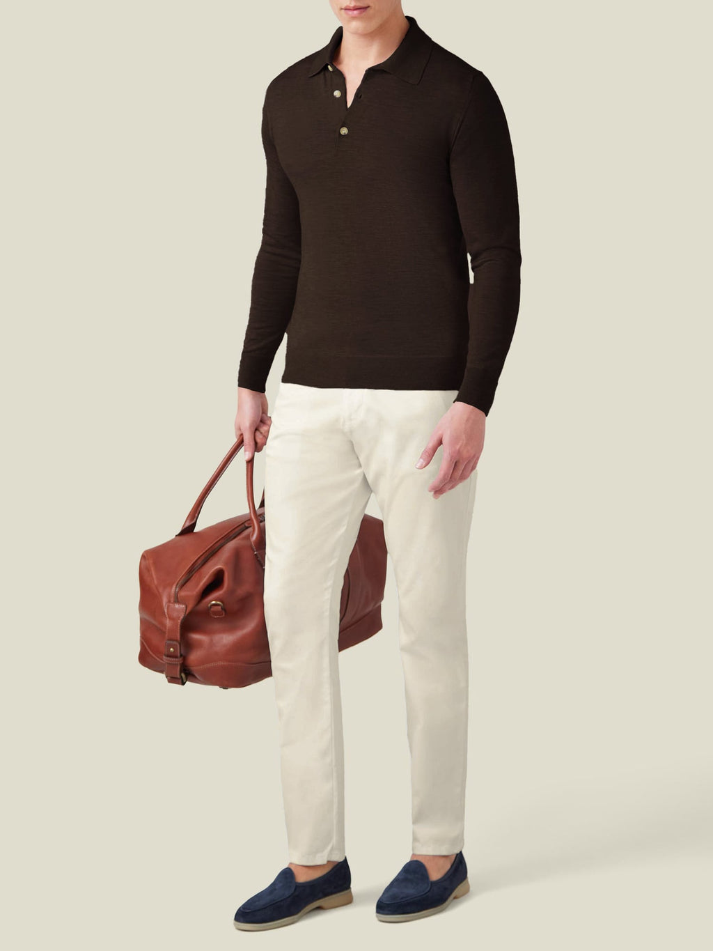 Model wears the Fine Silk Cashmere Polo in Chocolate Brown with off-white trousers and a leather weekender bag.