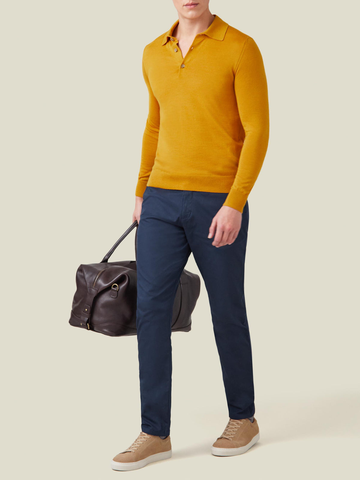 Man wearing the Mustard Fine Silk Cashmere Polo with navy trousers and beige sneakers, holding a brown leather bag.