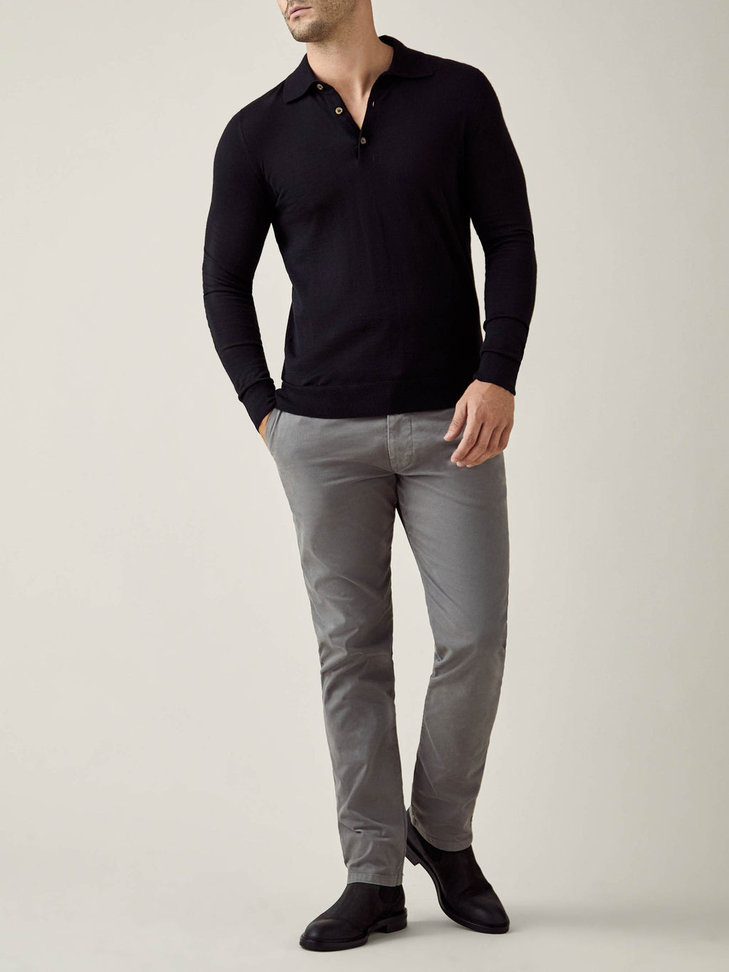Model wearing the long-sleeve Fine Silk Cashmere Polo in black, styled with grey trousers and black boots.