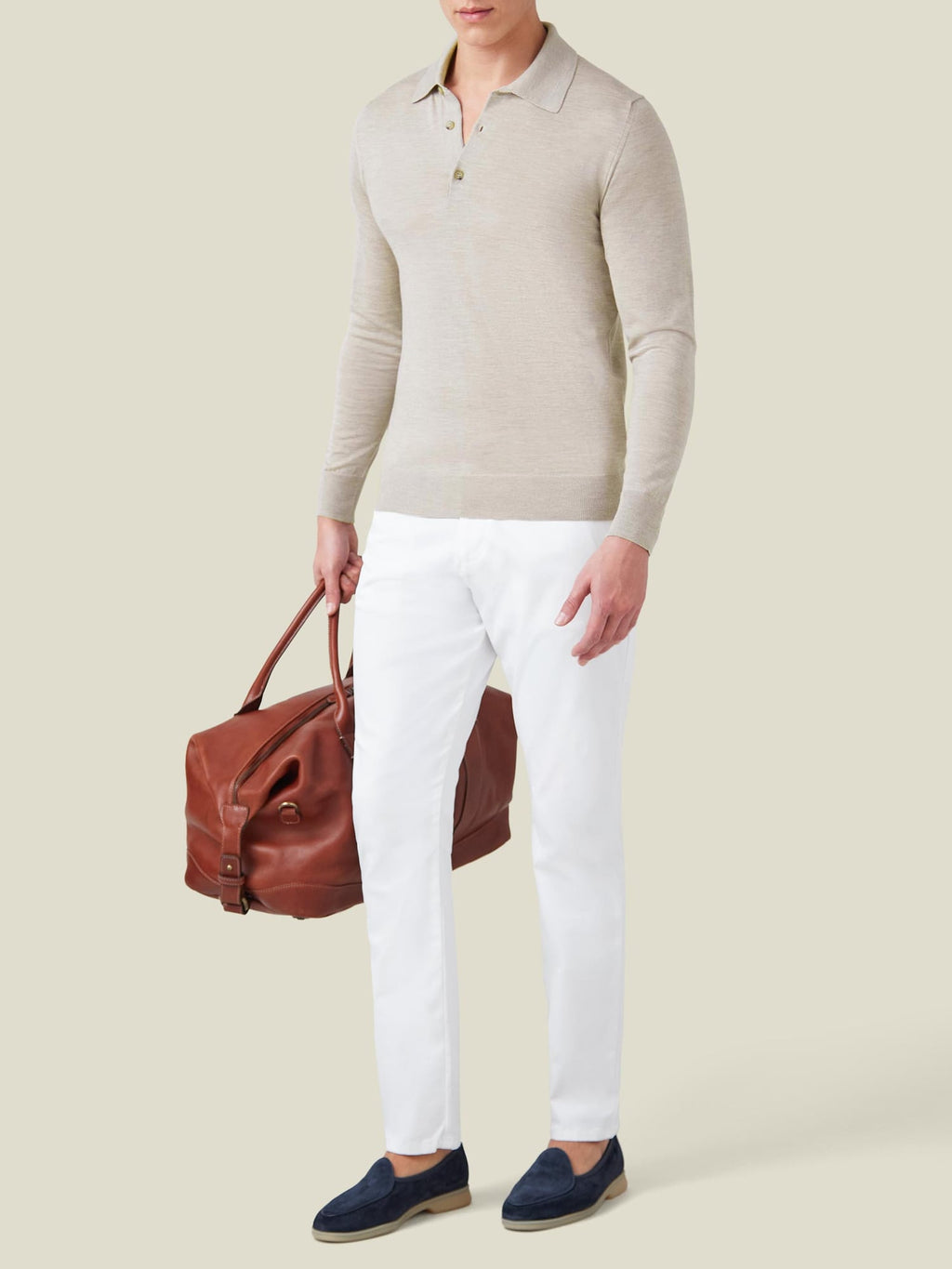 Man wearing the Luca Faloni Oatmeal Fine Silk Cashmere Polo with white trousers, navy loafers, and a brown leather bag.