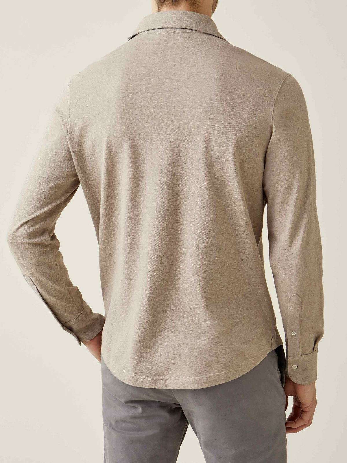 Back of a model wearing the long-sleeved Brera Piqué Polo Shirt in Oatmeal, showing its relaxed fit and cuffed sleeves.