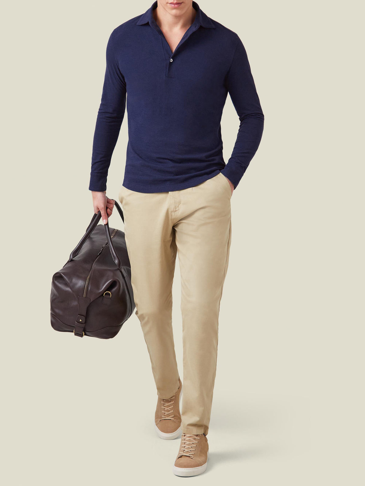 A model wears the Navy Blue Brera Piqué Polo Shirt with beige chinos and sneakers, holding a brown leather bag.