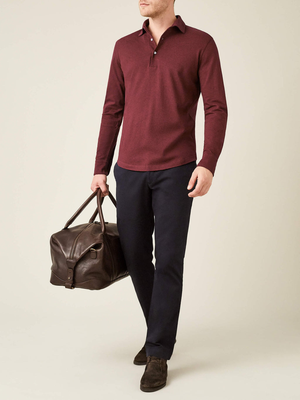Model wears the Lava Red Brera Piqué Polo Shirt from Luca Faloni, styled with dark trousers and a brown leather travel bag.