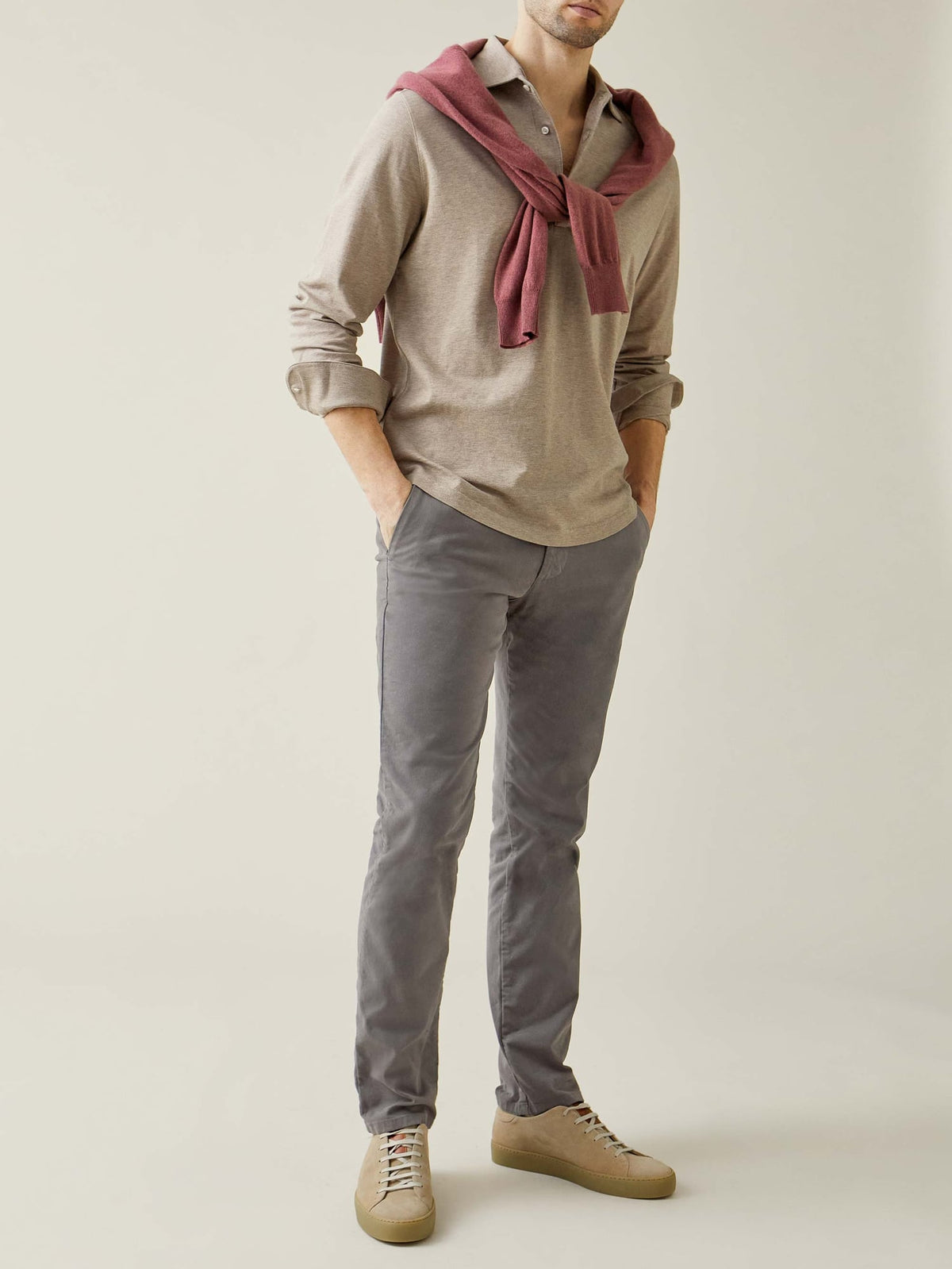 Full-body shot of a model wearing the oatmeal Brera Piqué Polo Shirt with grey trousers and a red sweater over his shoulders.