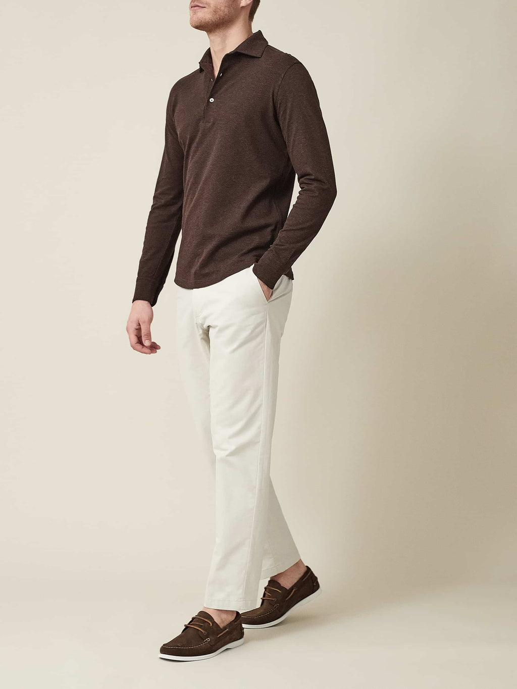 Model wears the Brera Piqué Polo Shirt in Chocolate Brown with cream trousers and brown loafers against a neutral background.