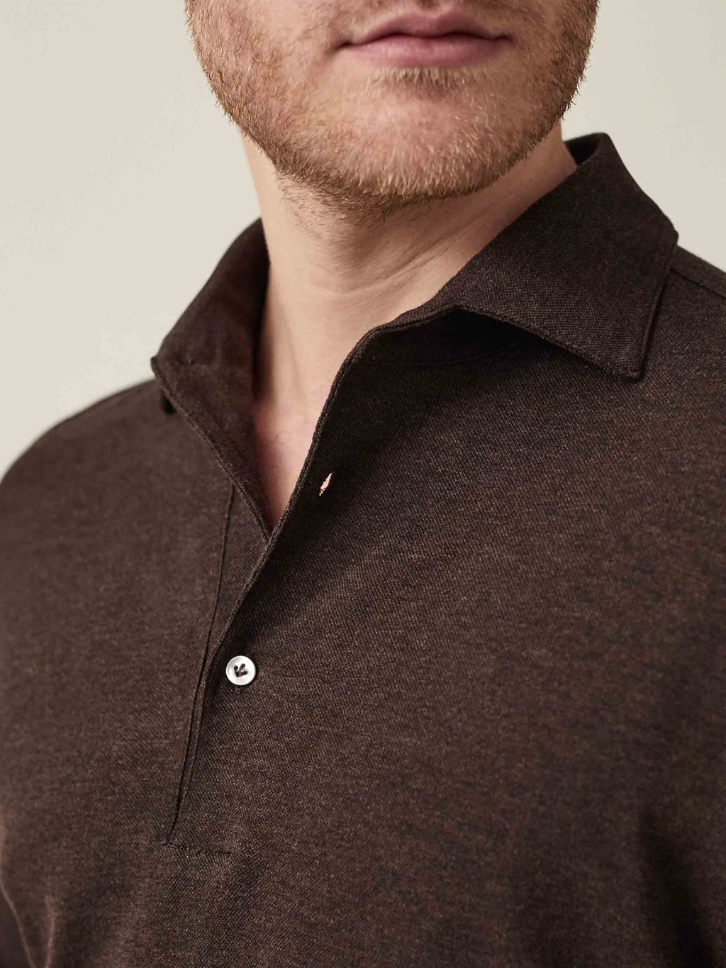A close-up of a model wearing the Brera Piqué Polo Shirt in chocolate brown, showing the one-piece collar and fabric texture.