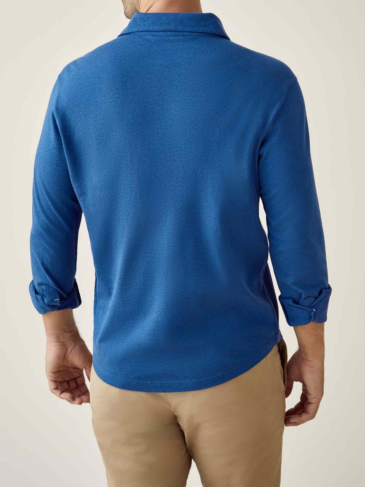 Back view of a model wearing the Brera Piqué Polo Shirt in royal blue with the sleeves rolled up, paired with khaki chinos.
