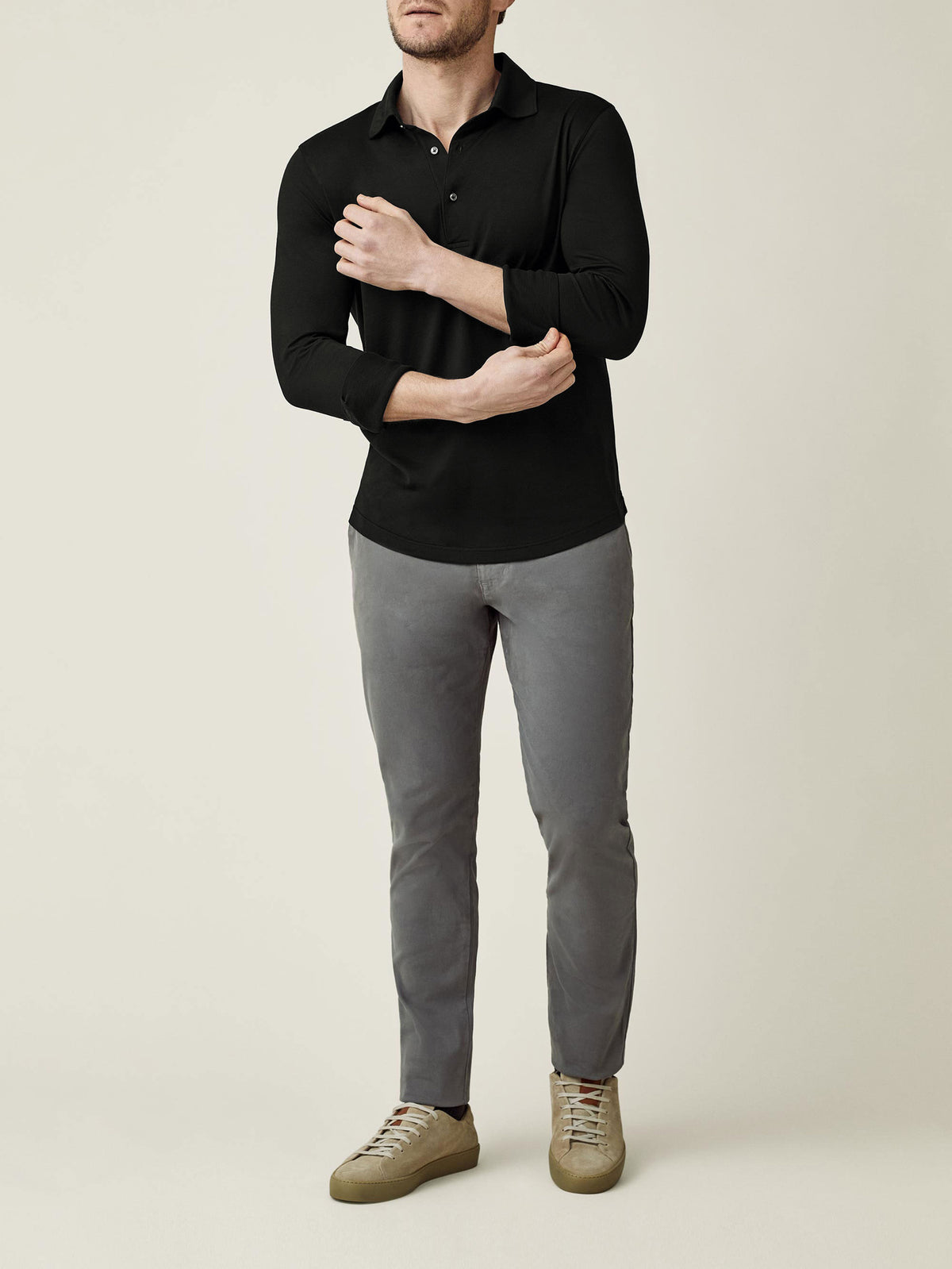 Model wearing the long-sleeved Amalfi Silk-Cotton Polo Shirt in black with grey trousers, adjusting the cuff.