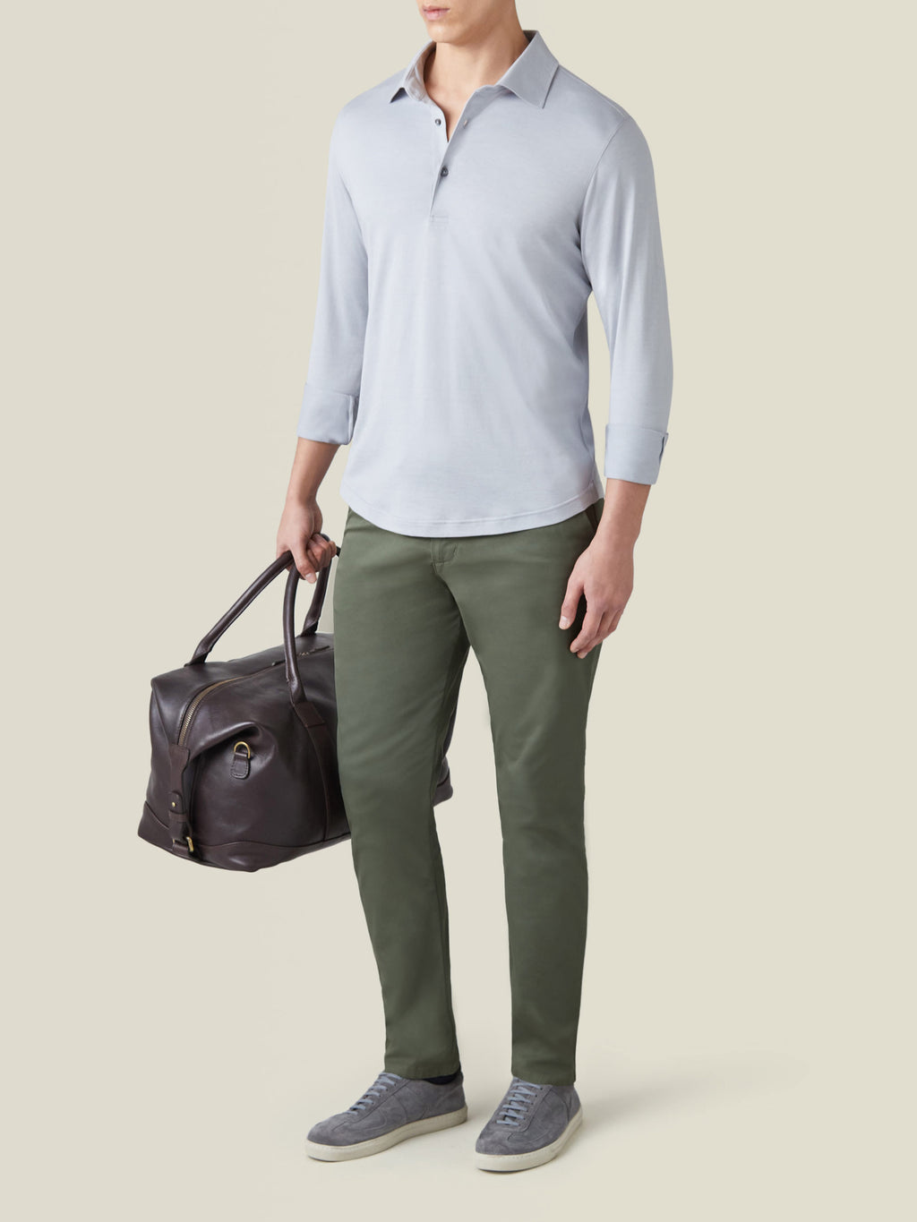 Front view of a model wearing the light grey Amalfi Silk-Cotton Polo with olive chinos and a leather weekender bag.