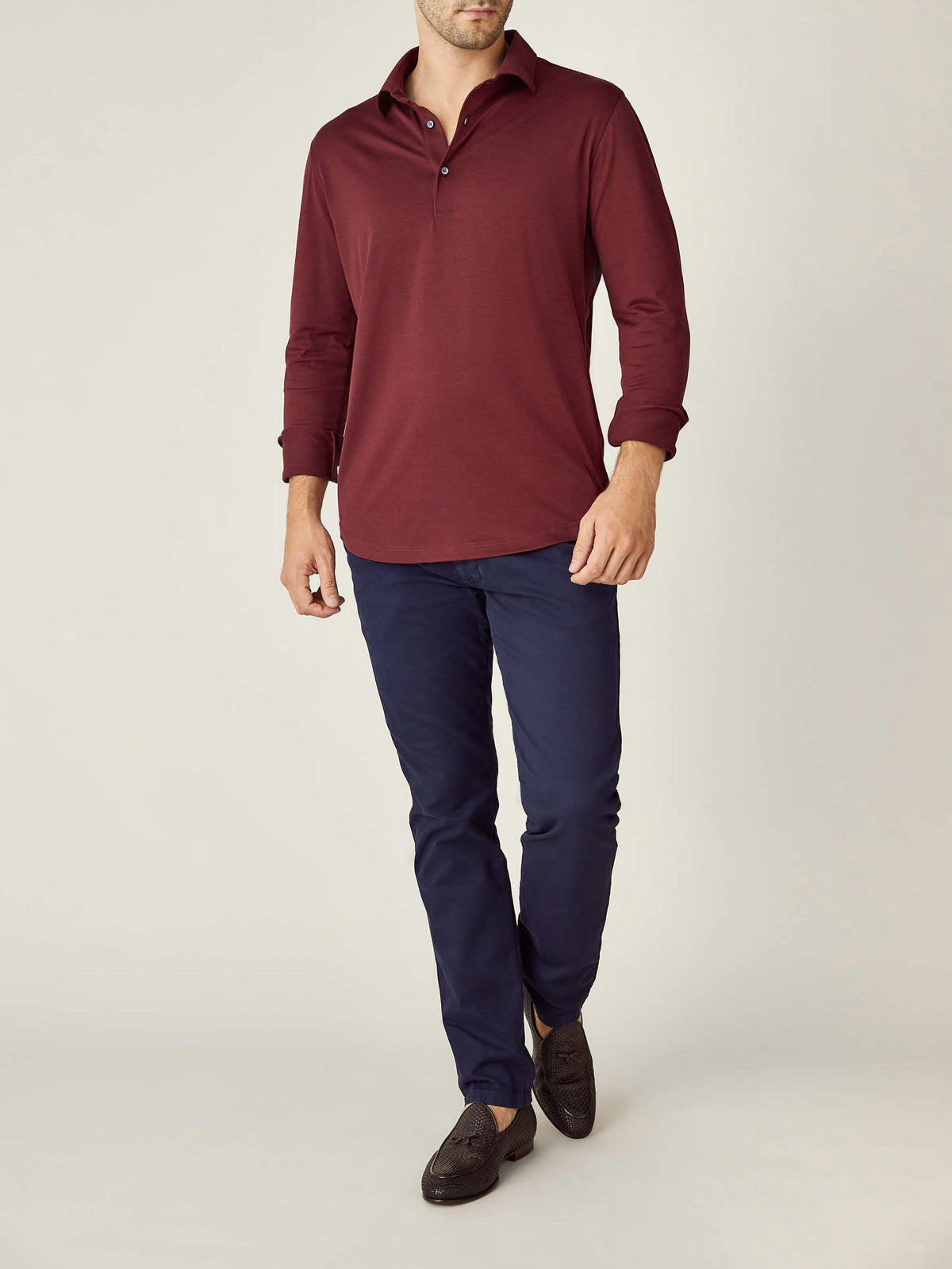 Model wearing the Amalfi Silk-Cotton Polo Shirt in Lava Red with navy trousers and dark loafers against a studio background.