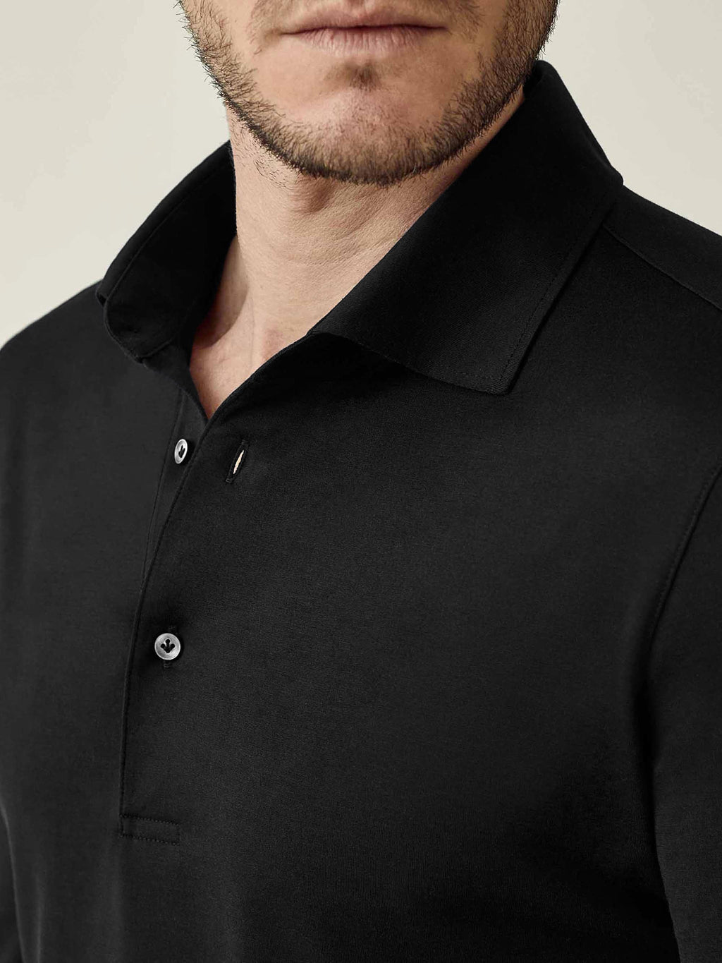 Close-up of the black Amalfi silk-cotton polo shirt, detailing the collar and mother of pearl buttons.