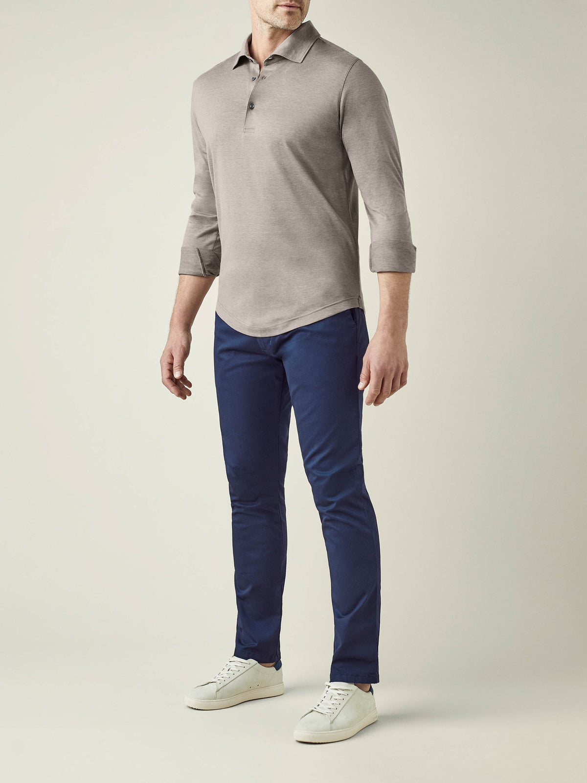 A model wears the Amalfi Silk-Cotton Polo Shirt in Nocciola Brown, styled with navy trousers and white sneakers.