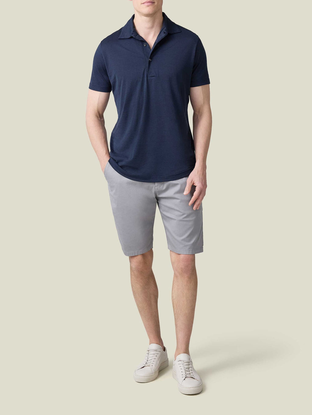 Full look of a model wearing the Short-sleeved Silk-Cotton Polo in midnight blue with grey shorts and white trainers.