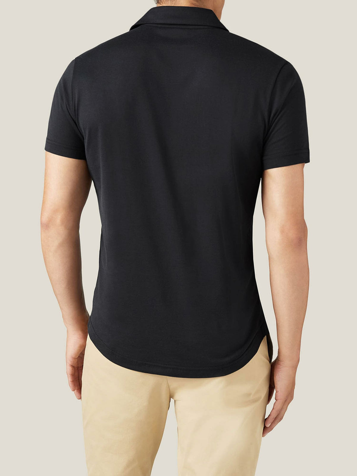 Back view of a model wearing a black silk-cotton polo shirt, showcasing the relaxed fit and rounded hemline.