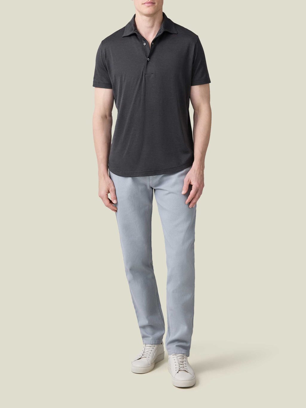 Full-length view of a model wearing a charcoal grey short-sleeved silk-cotton polo with light blue chinos and white trainers.