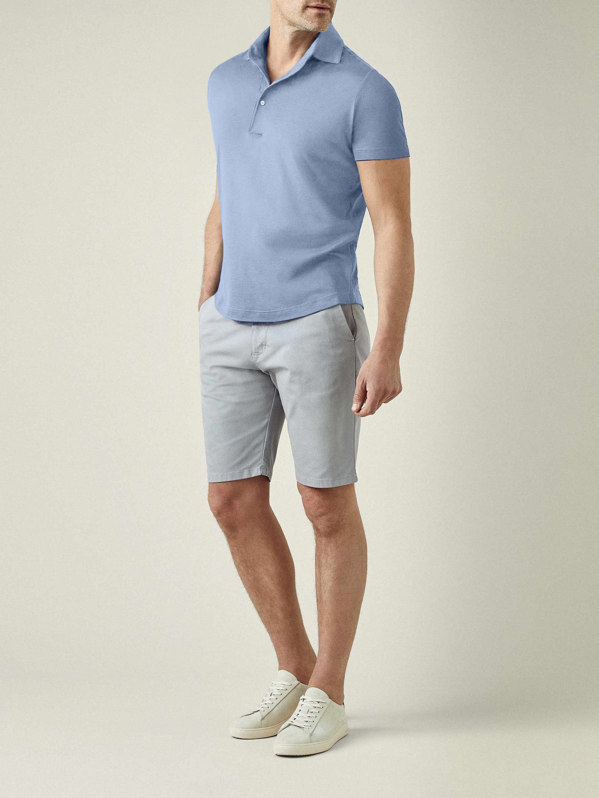 Model wears the Luca Faloni light blue short-sleeved silk-cotton polo with grey shorts and white trainers.