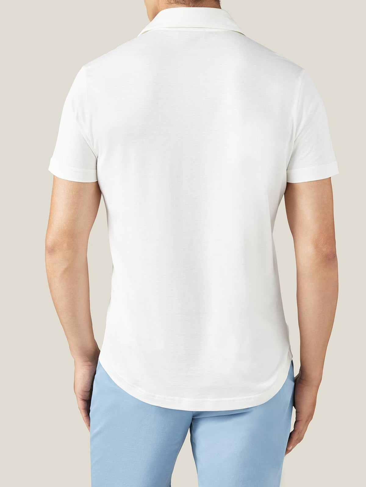 Back view of a man wearing a white short-sleeved silk-cotton polo shirt, showing its relaxed fit and curved hem.