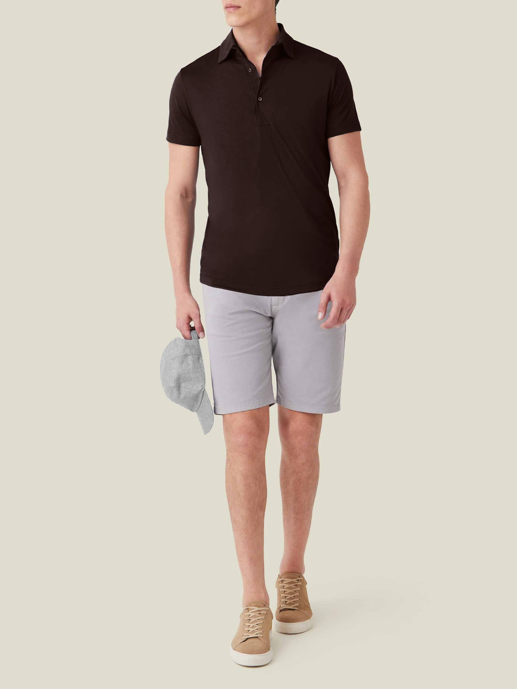 A model wearing the Luca Faloni Short-sleeved Silk Cotton Polo in chocolate brown with light grey shorts and beige trainers.