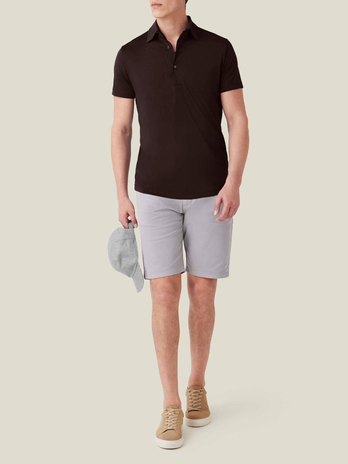 A model wearing the Luca Faloni Short-sleeved Silk Cotton Polo in chocolate brown with light grey shorts and beige trainers.