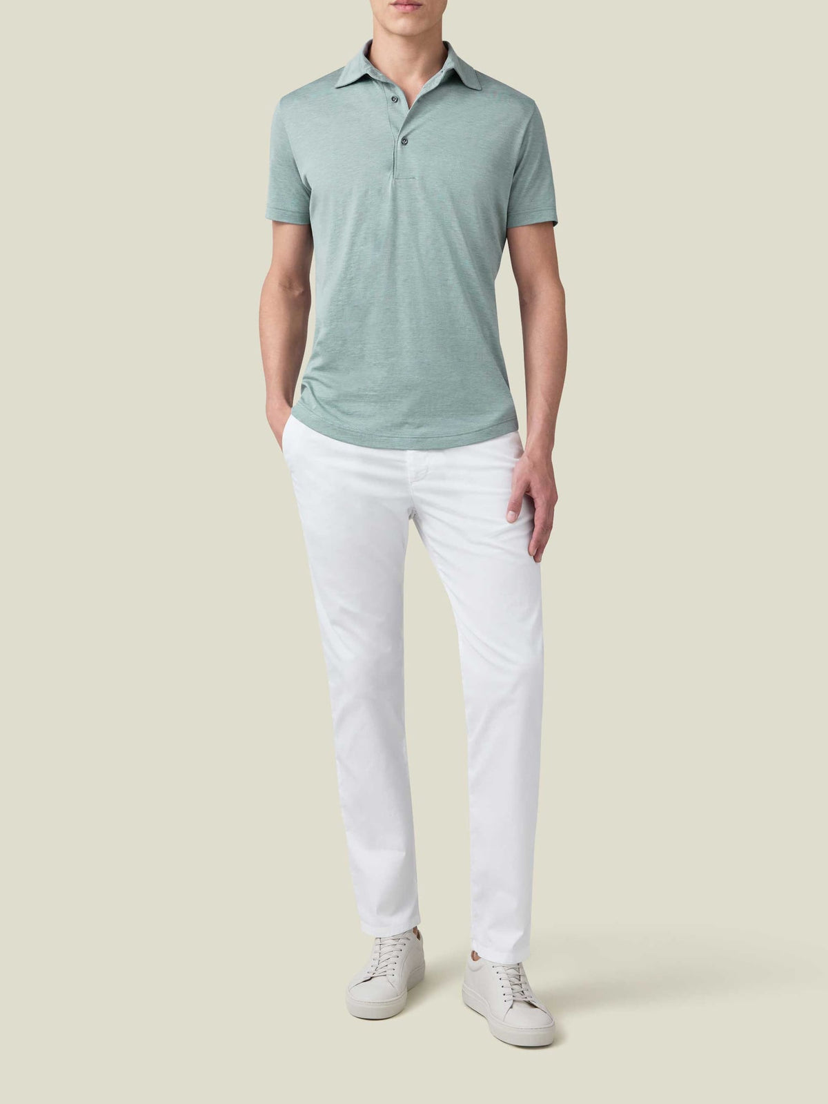 Front view of a model wearing the Luca Faloni marine green silk-cotton polo with white trousers and white sneakers.