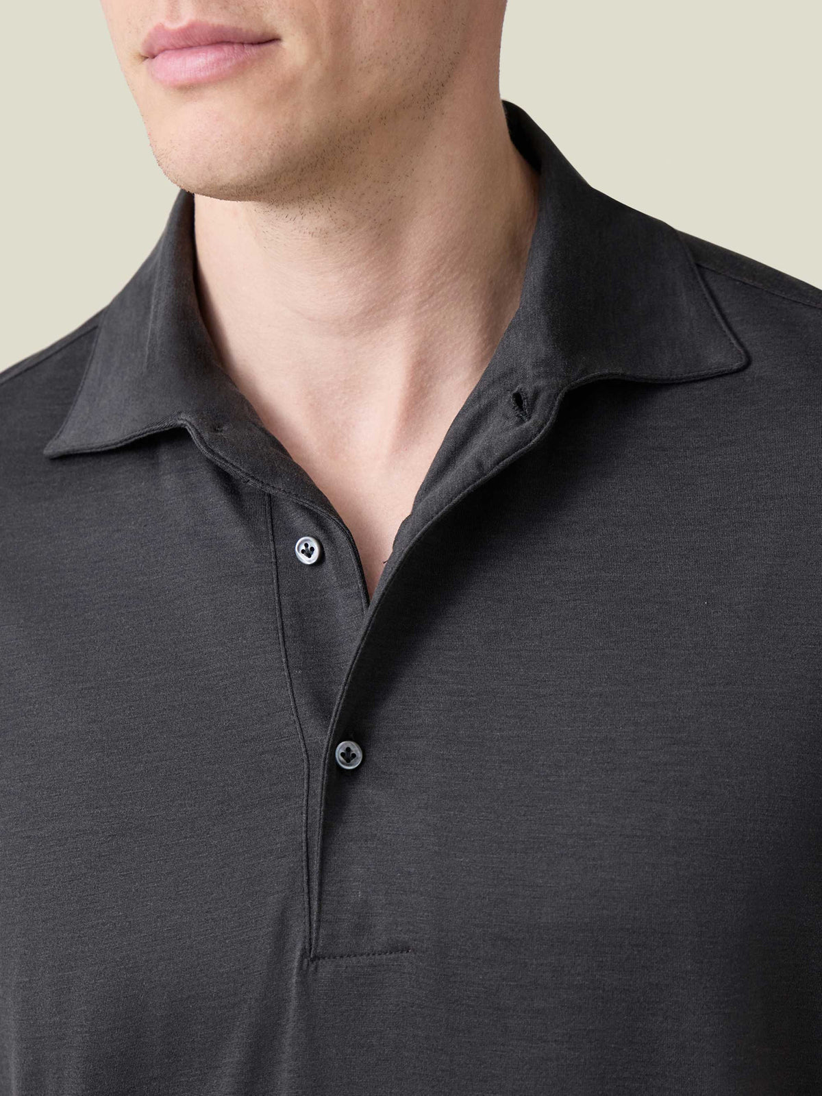 A close-up of the charcoal grey silk-cotton polo, showcasing the one-piece collar and mother of pearl buttons.
