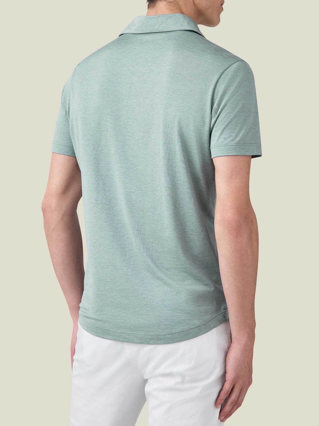Model wears the Marine Green Silk-Cotton Polo shirt, seen from behind to showcase the relaxed fit and rounded hemline.