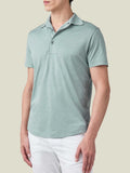 Side profile of a model wearing a marine green silk-cotton short-sleeved polo shirt paired with white trousers.