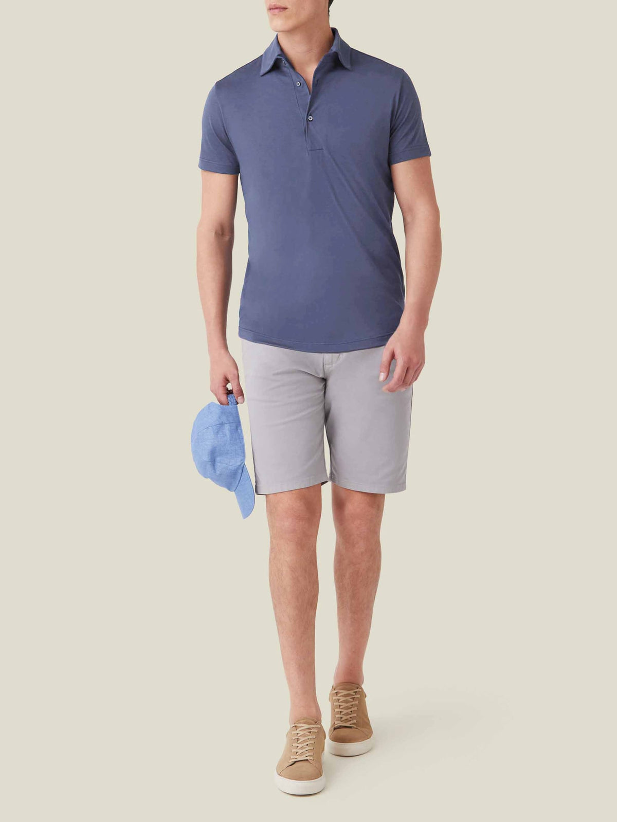 Model wears the Ocean Blue Short-Sleeved Silk-Cotton Polo paired with light grey shorts and holding a light blue cap.