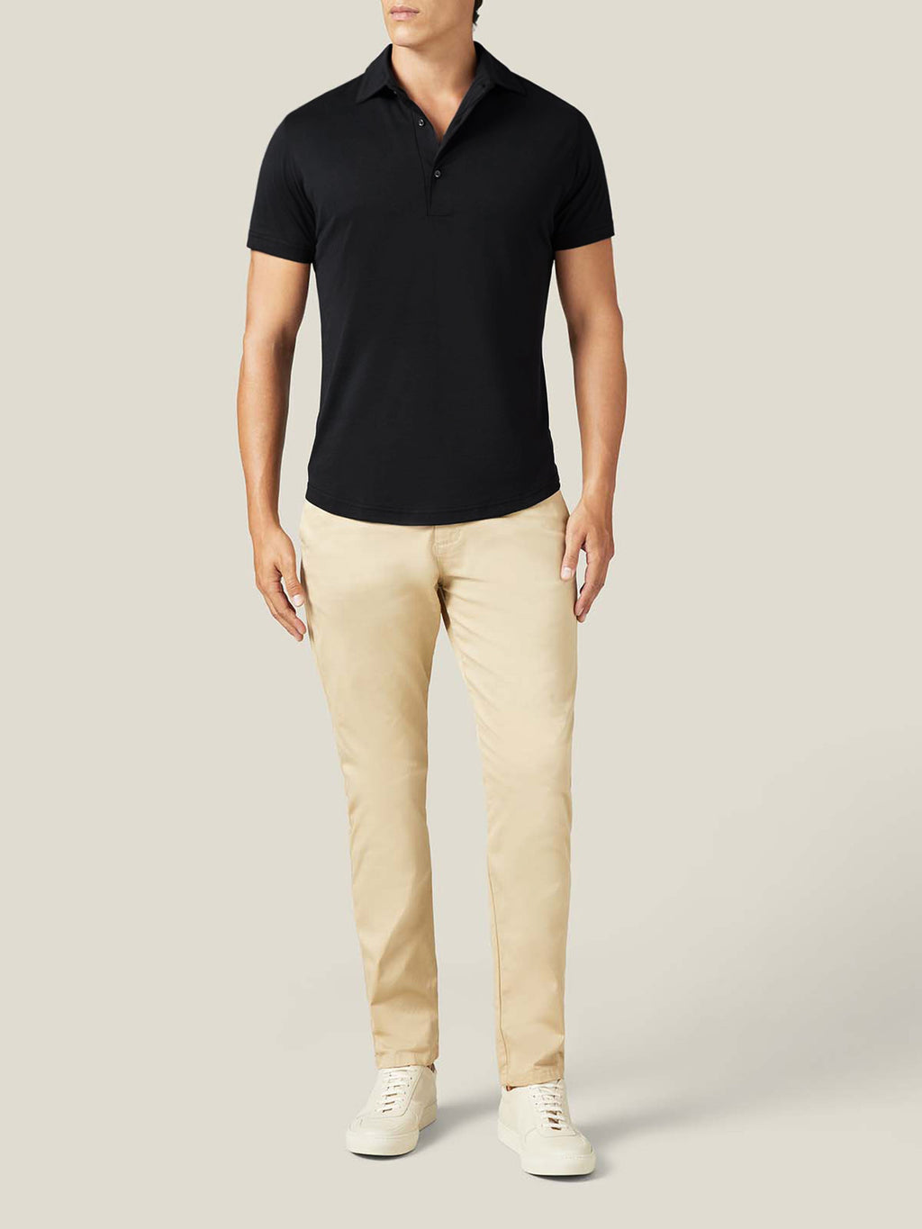 Model from the front wearing a black silk-cotton short-sleeved polo, styled with beige chinos and white sneakers.