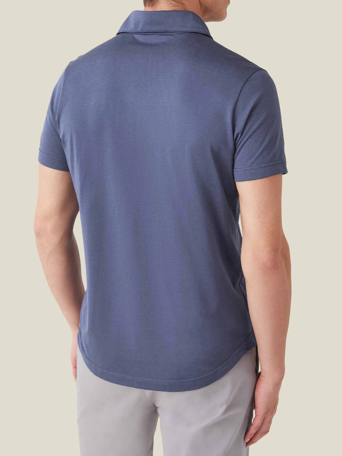 Back view of a man wearing the ocean blue silk-cotton polo, showcasing its relaxed fit and rounded hem.