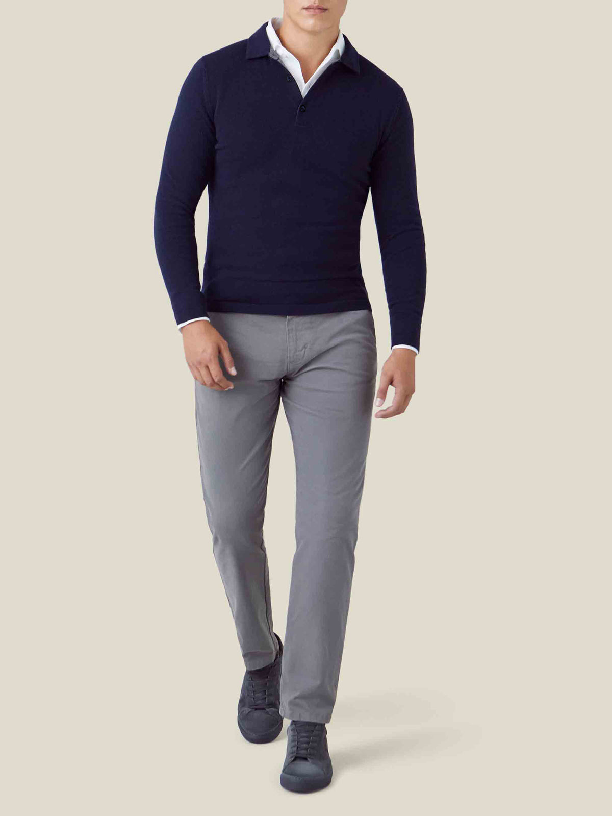 Man wearing a midnight blue cashmere polo sweater, layered over a white shirt and paired with grey trousers.
