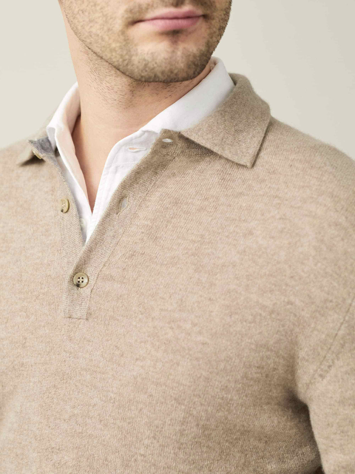 Close-up of the collar and fine-knit texture of the camel beige cashmere polo sweater, worn by a model over a white shirt.