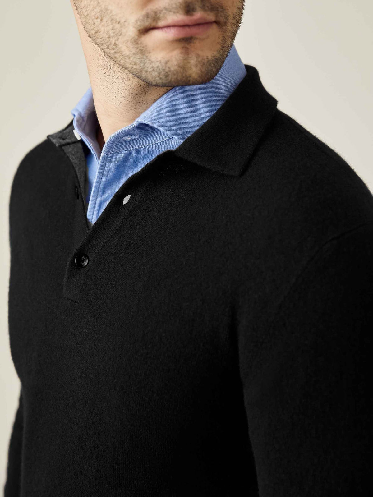 Detailed close-up of the black cashmere polo sweater layered over a light blue collared shirt, highlighting the collar.