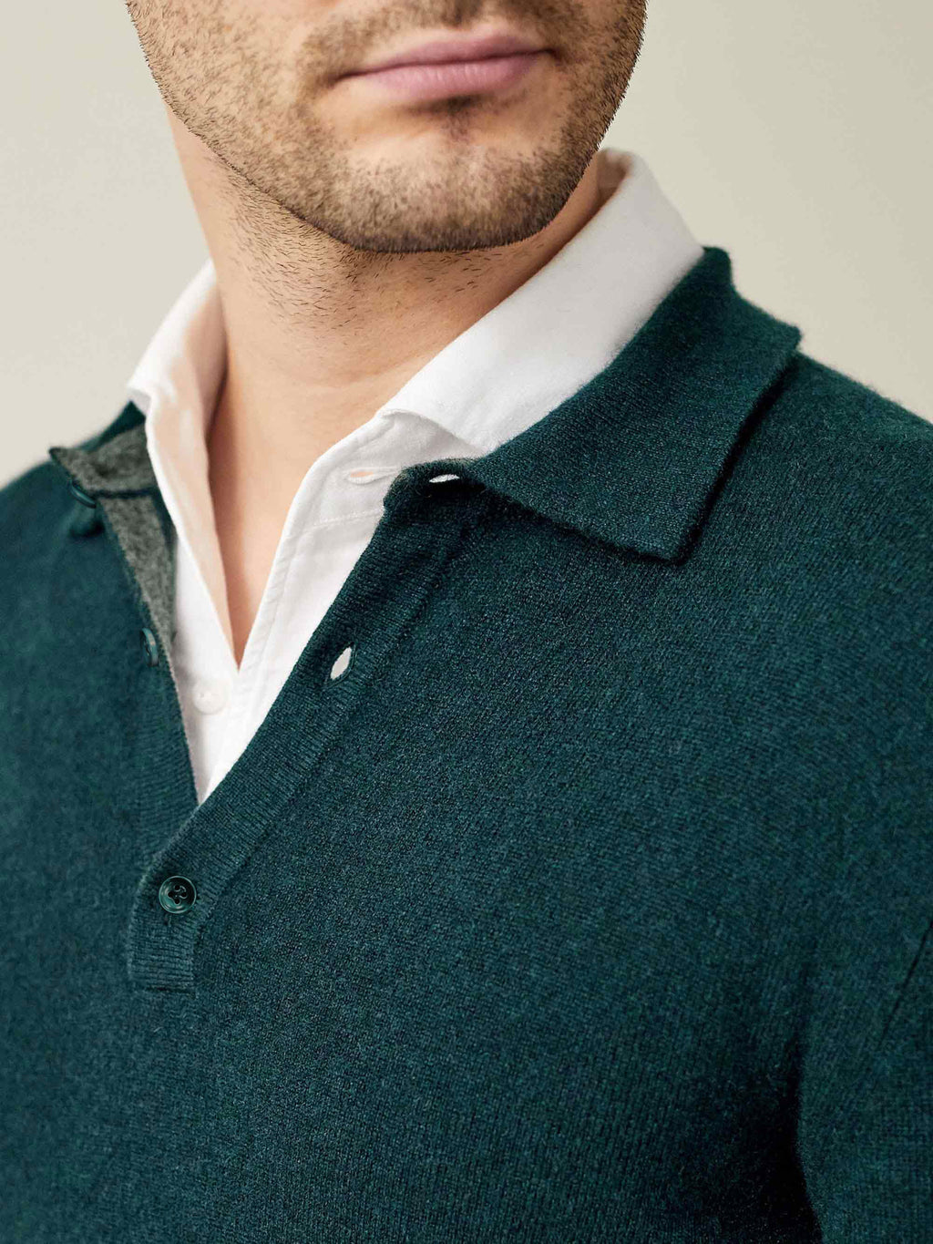 Close-up on the collar detail of a man wearing a forest green cashmere polo sweater styled over a white shirt.