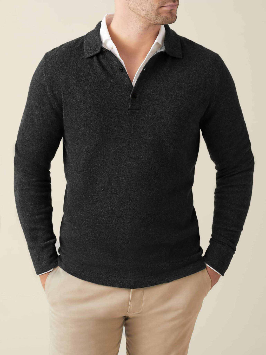 Front view of a man wearing a charcoal grey cashmere polo sweater layered over a white shirt and beige chinos.