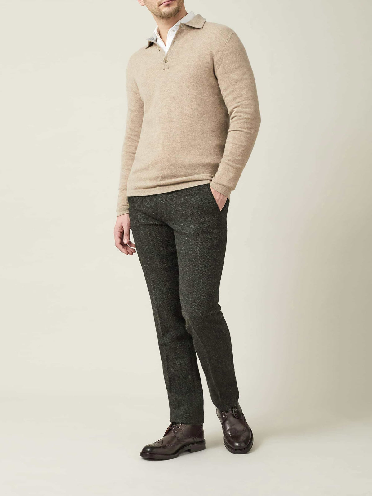 Model wears the Luca Faloni camel beige cashmere polo sweater with dark green trousers and brown leather derby shoes.