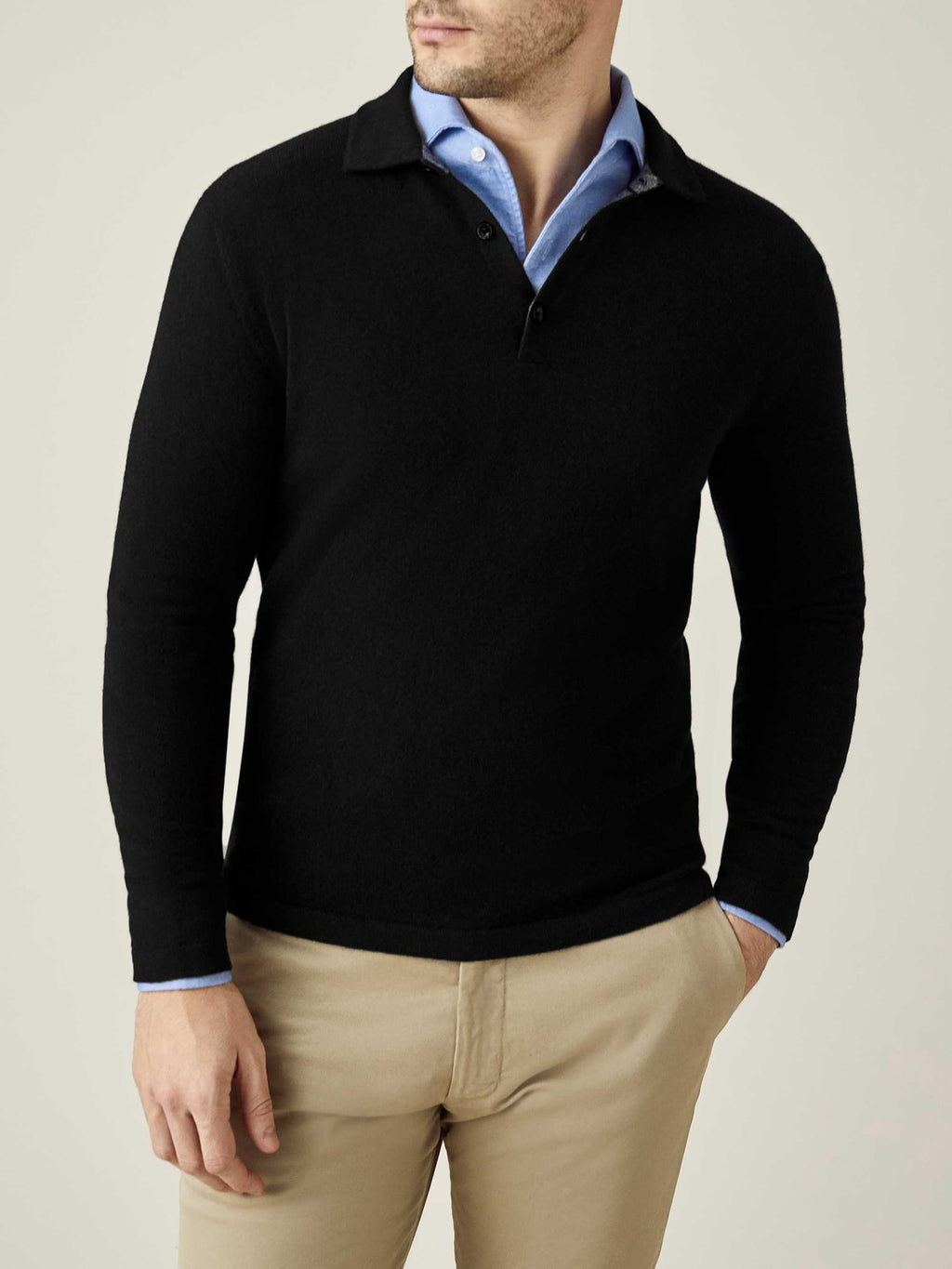 A man models the Luca Faloni Black Cashmere Polo Sweater, layered over a light blue shirt and styled with beige chinos.
