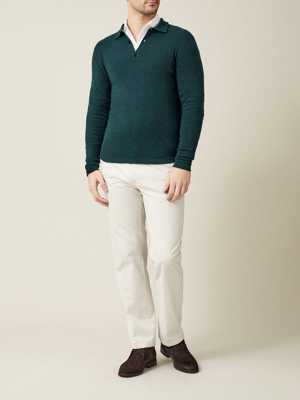 A man models the forest green cashmere polo sweater, layered over a white shirt with cream trousers and brown shoes.
