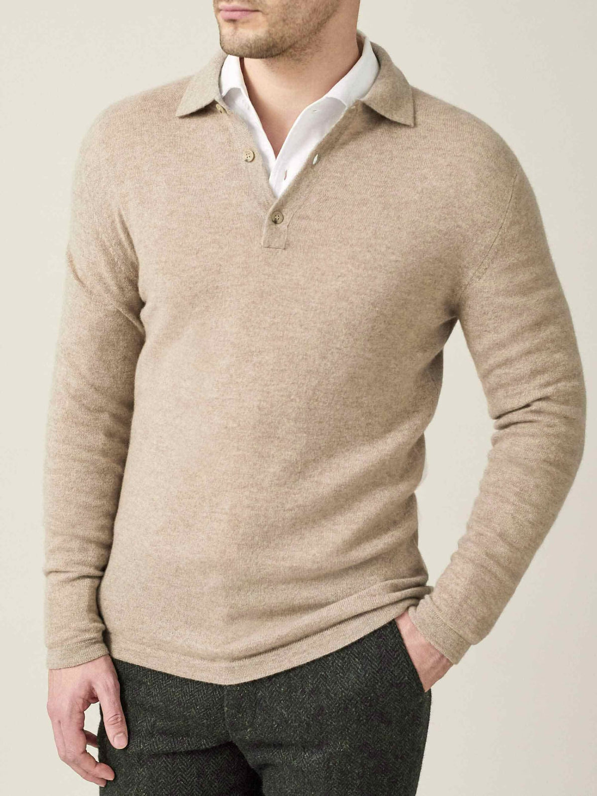 A model wears the Cashmere Polo Sweater in camel beige, layered over a white collared shirt and dark trousers.