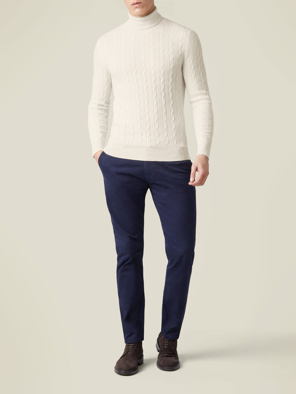 Man wearing the Luca Faloni Cable Knit Roll Neck in Ivory, styled with navy trousers and brown shoes.
