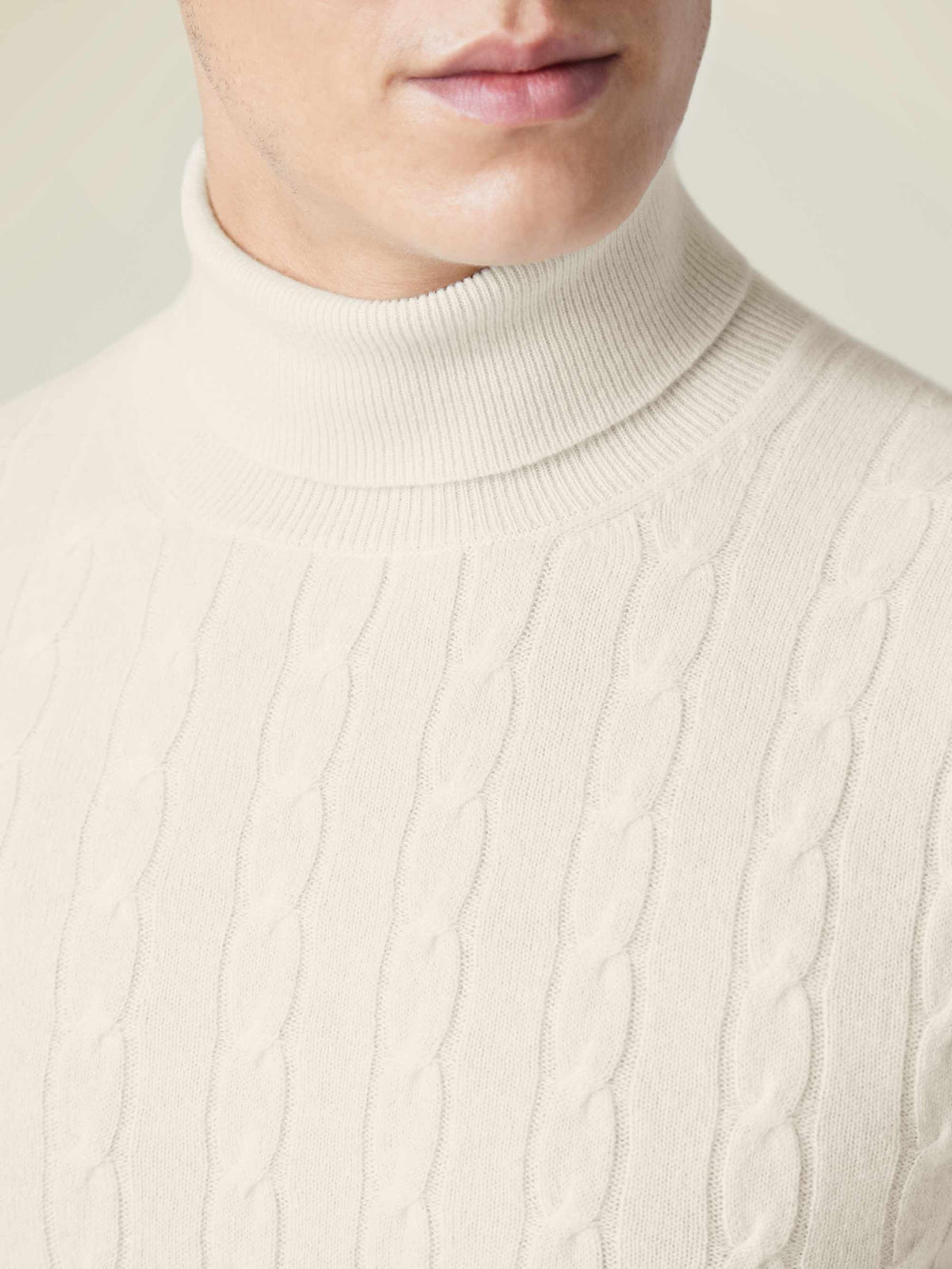 Close-up detail of the ivory Cable Knit Roll Neck, highlighting the luxurious cashmere and textured cable knit pattern.