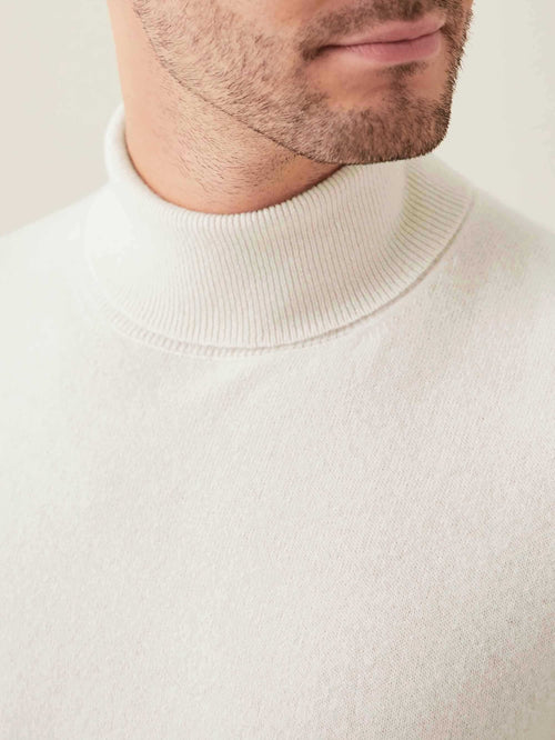 A close-up view of a man's neck and jaw, showing the detailed ribbed collar of the ivory cashmere roll neck sweater.