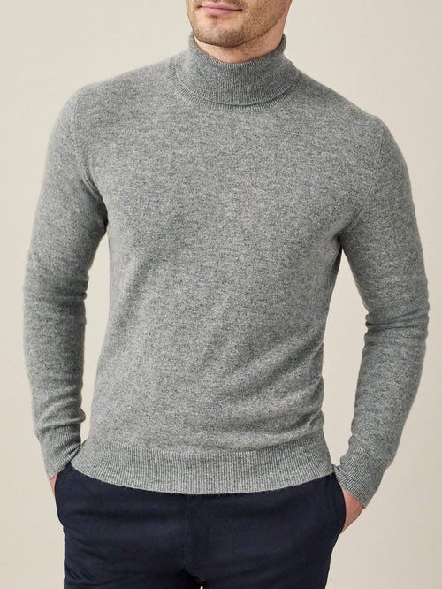A man models the Luca Faloni Pure Cashmere Roll Neck in Dolomiti Grey, a versatile light grey sweater.