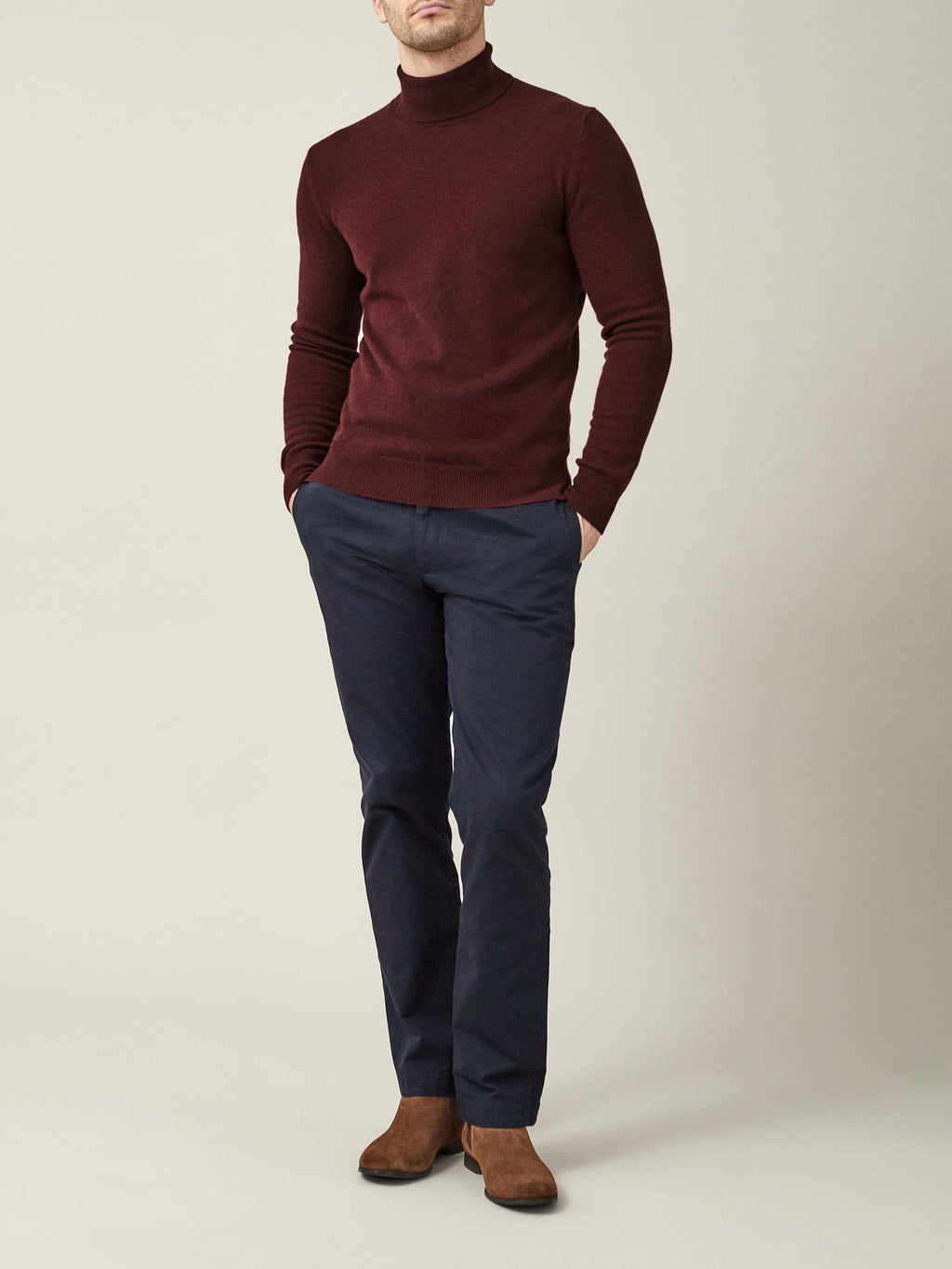 A man models the Luca Faloni Lava Red Cashmere Roll Neck, styled with navy trousers and brown suede boots.