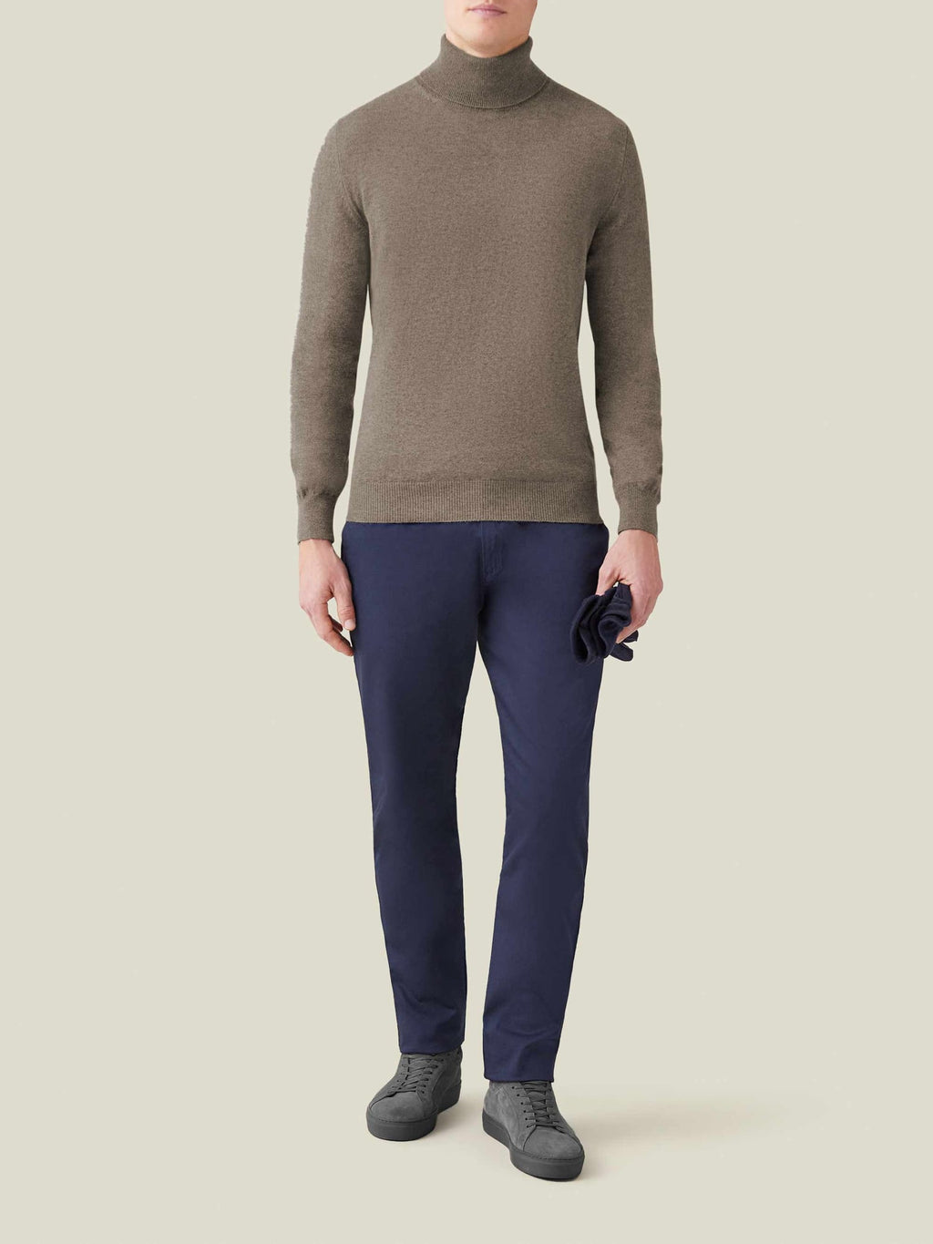 Model wears the Nocciola Brown Cashmere Roll Neck, styled with navy trousers and grey sneakers, in a full-length photo.